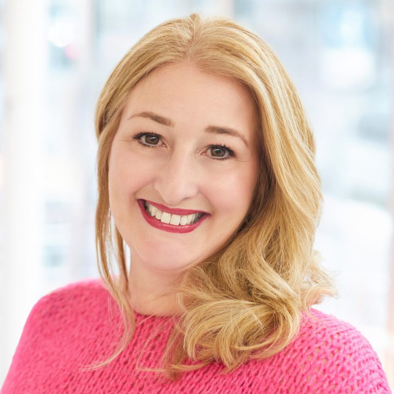 Ina Rottmüller Portrait Eine lächelnde Frau mit blonden Haaren trägt ein pinkes Oberteil.