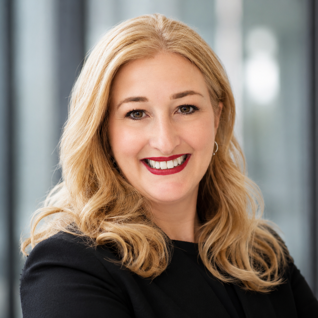 Strategic Advisory für Unternehmer & Geschäftsführungen Lächelnde Frau mit blonden Haaren und schwarzer Bluse vor einem modernen Hintergrund.